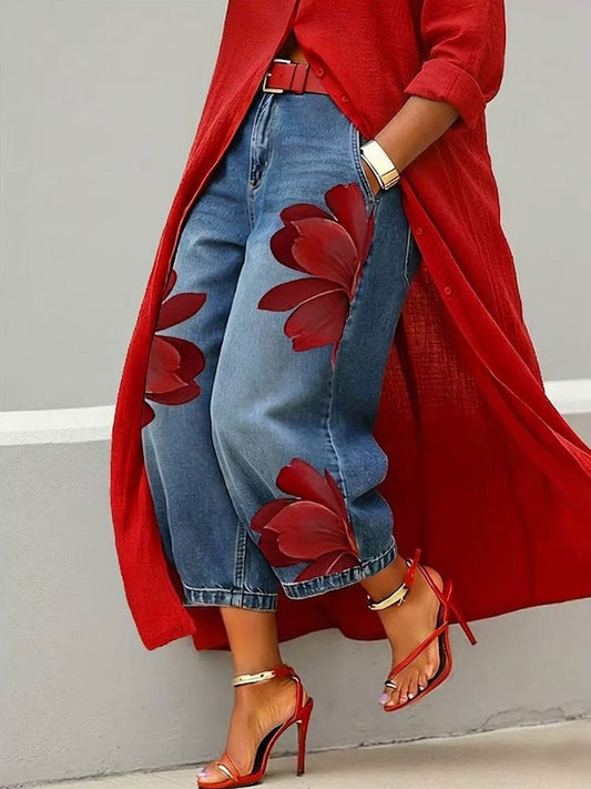 Vaqueros azules de pierna ancha con flores rojas de gran tamaño, vistos de cerca con el bajo por encima del tobillo.
