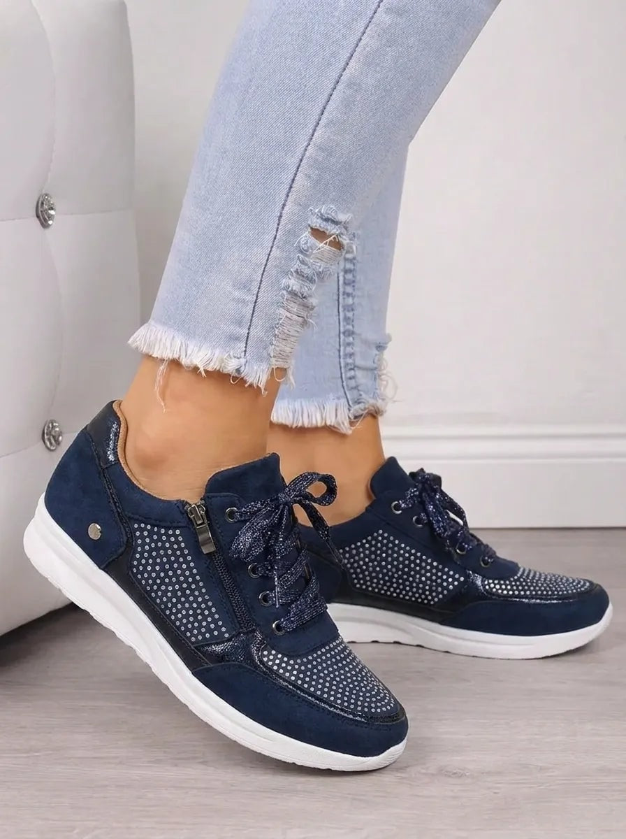 Vista lateral de las zapatillas azul marino colocadas sobre el suelo, con detalles brillantes en los paneles y suela blanca.