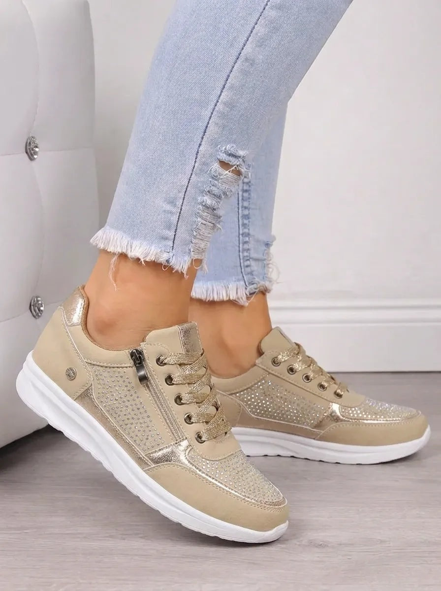 Par de zapatillas casual en tono dorado claro, con cordones, cremalleras laterales y detalles decorativos brillantes.