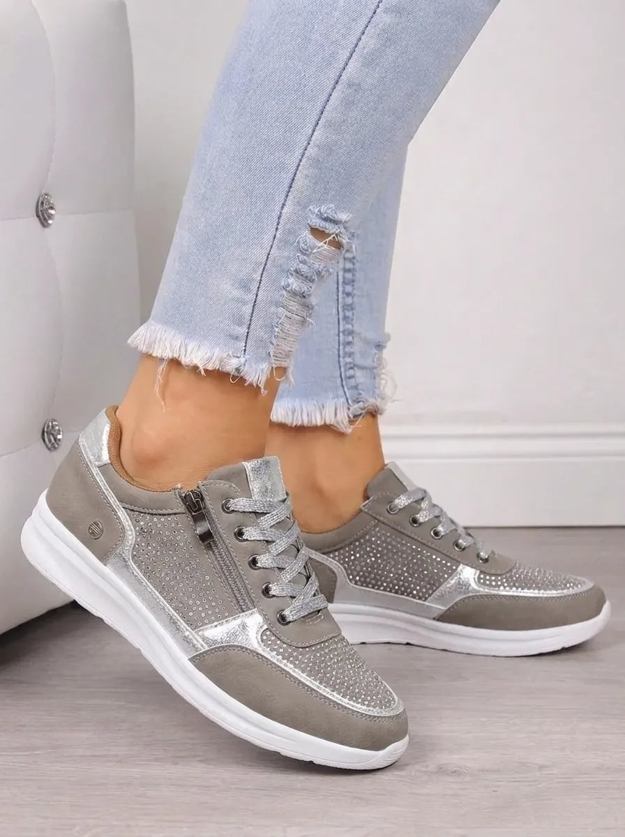 Zapatillas casual en tono gris plateado, mostradas de perfil con cordones, cremalleras laterales y suela blanca.