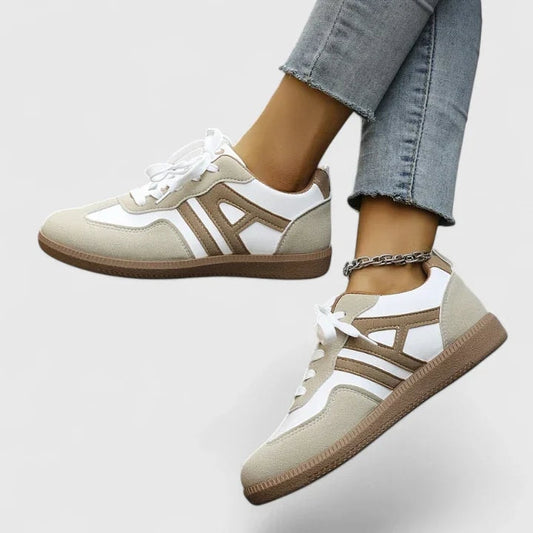 Zapatillas casuales de cordones en tonos beige y blanco, mostradas en los pies con paneles laterales en contraste y suela plana marrón.