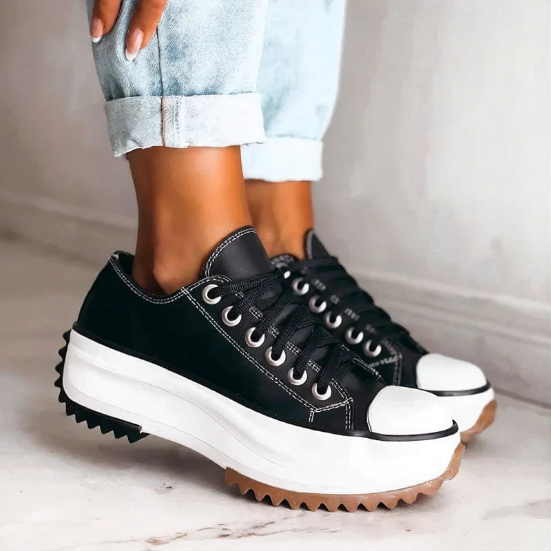 Zapatillas negras de plataforma con punteras blancas, cordones, costuras visibles y suelas dentadas en tonos negro y marrón.