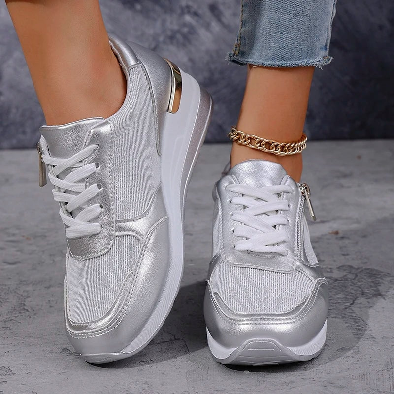 Par de zapatillas de plataforma plateadas visto de frente y de perfil, con cordones blancos y cremalleras laterales claramente visibles.