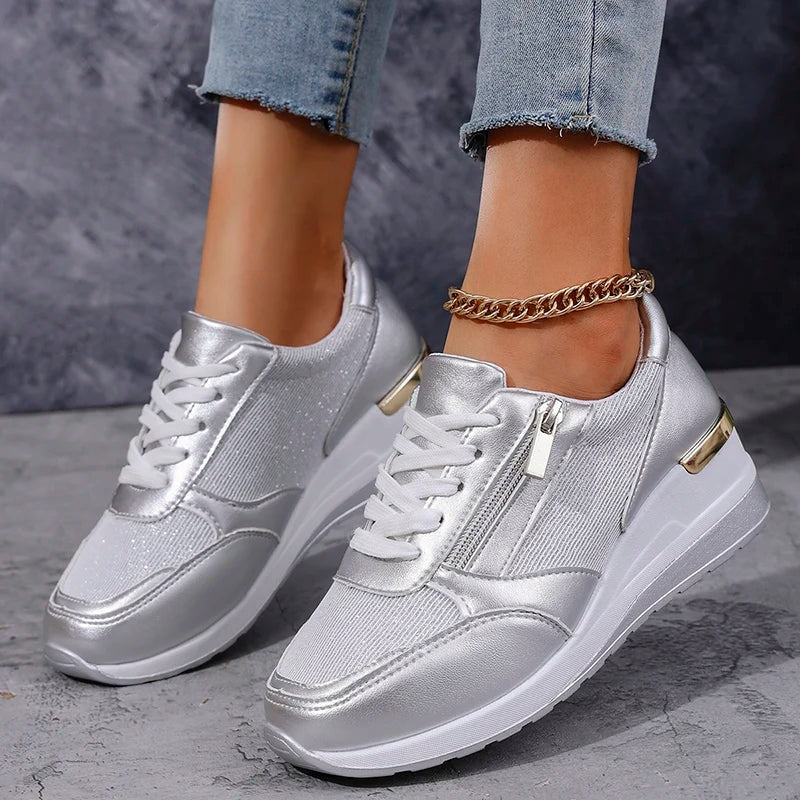 Zapatillas plateadas de plataforma en una vista de tres cuartos, mostrando los paneles laterales, los cordones blancos y los detalles dorados del talón.