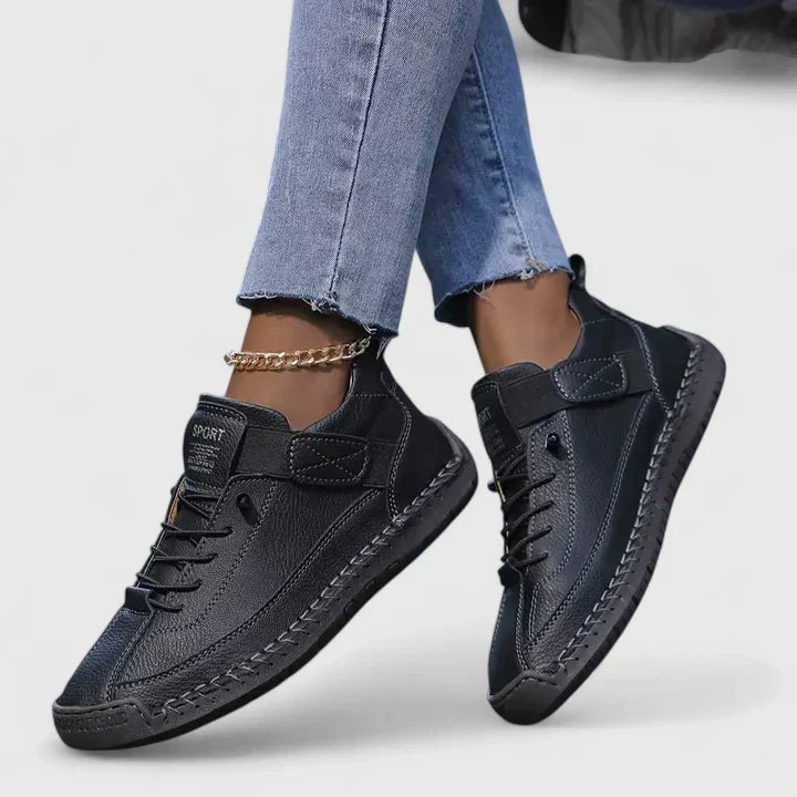 Zapatillas planas negras con cordones y cierre ajustable, mostradas en los pies con un diseño casual.