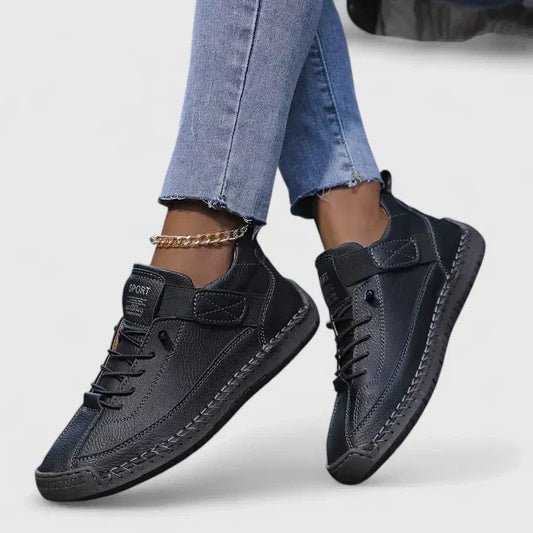 Zapatillas planas negras con cordones y cierre ajustable, mostradas en los pies con un diseño casual.