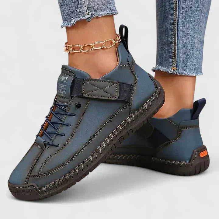 Zapatillas planas azul grisáceo con cordones, cierre ajustable y suela oscura, presentadas en los pies.