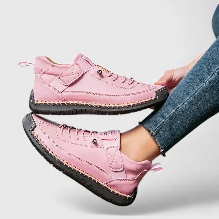Zapatillas planas rosas con cordones y cierre ajustable, mostradas en una vista lateral suspendida.