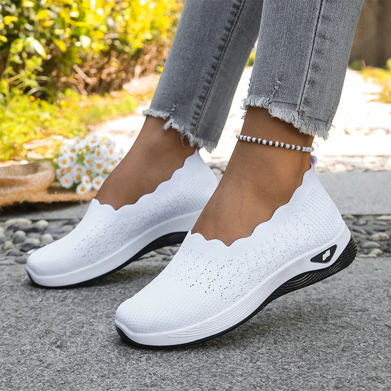 Zapatillas slip-on blancas con suelas oscuras y acolchadas, vistas en ambos pies.