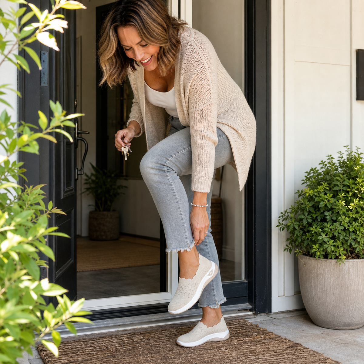 Mujer poniéndose una zapatilla slip-on beige junto a la entrada de su casa.