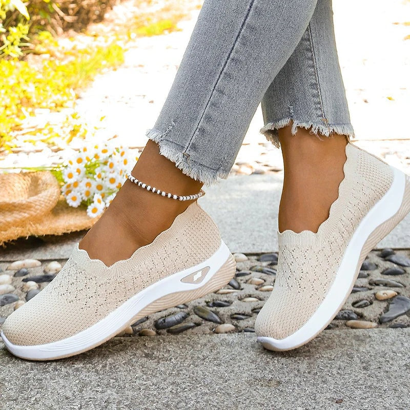 Vista cercana de ambos pies con zapatillas beige, mostrando los bordes ondulados y las suelas acolchadas.