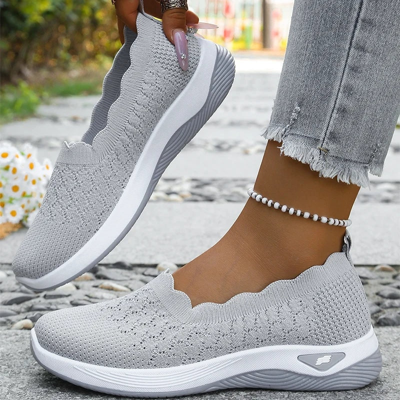 Zapatillas slip-on grises con tejido visible, borde ondulado y suelas blancas acolchadas.