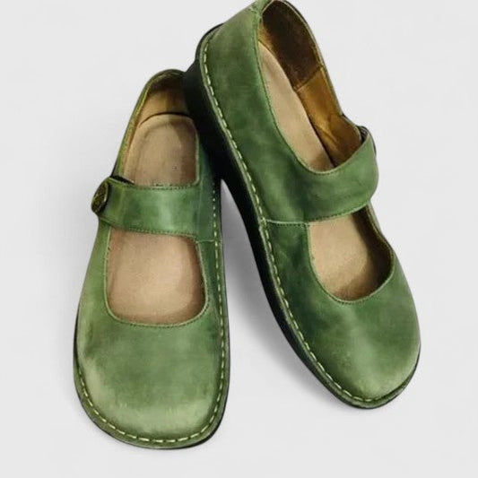 Par de zapatos Merceditas planos verdes, con puntera redondeada, tira ajustable sobre el empeine y costuras visibles en el borde.