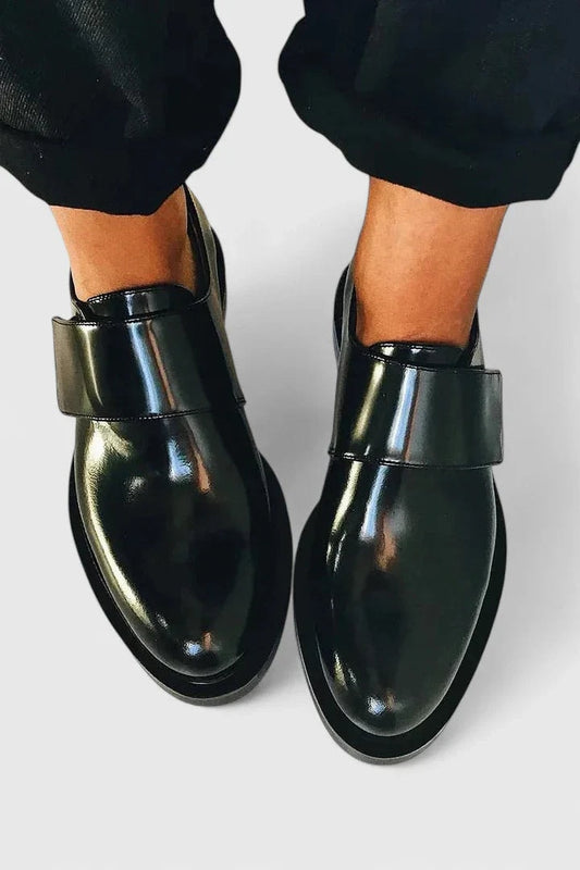 Zapatos planos negros de acabado brillante vistos desde arriba, con puntera redondeada y correa ancha sobre el empeine.