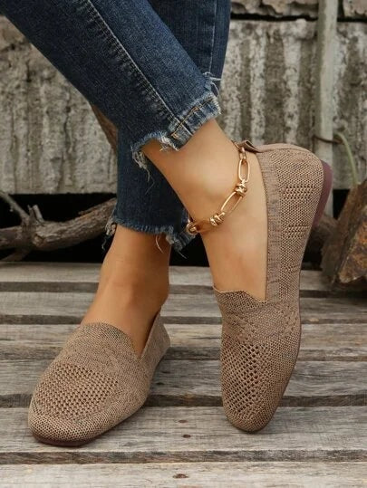Zapatos planos color topo mostrados de perfil sobre una superficie de madera, combinados con vaqueros.