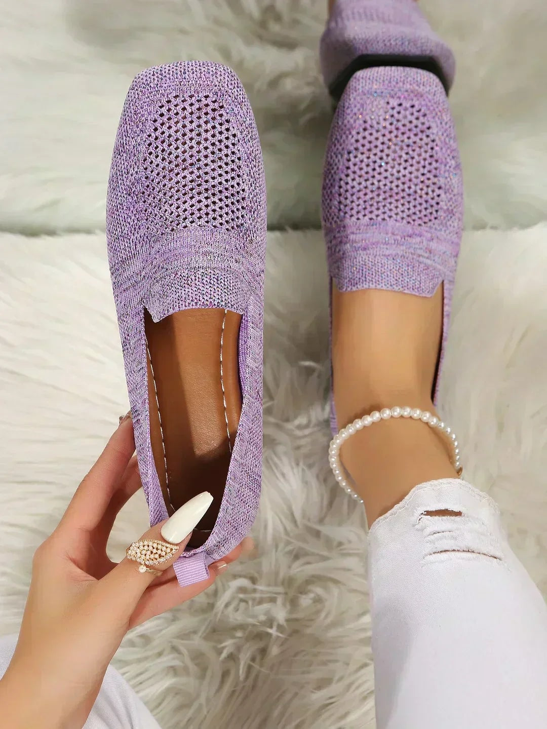 Zapatos planos lavanda con patrón calado, presentados desde arriba sobre una superficie mullida.